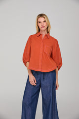 Woman wearing an orange shirt and blue jeans against a gray background