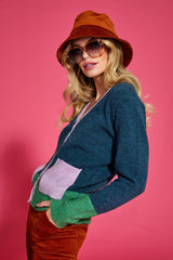 Woman wearing a colorful cardigan, corduroy pants and hat against a pink background