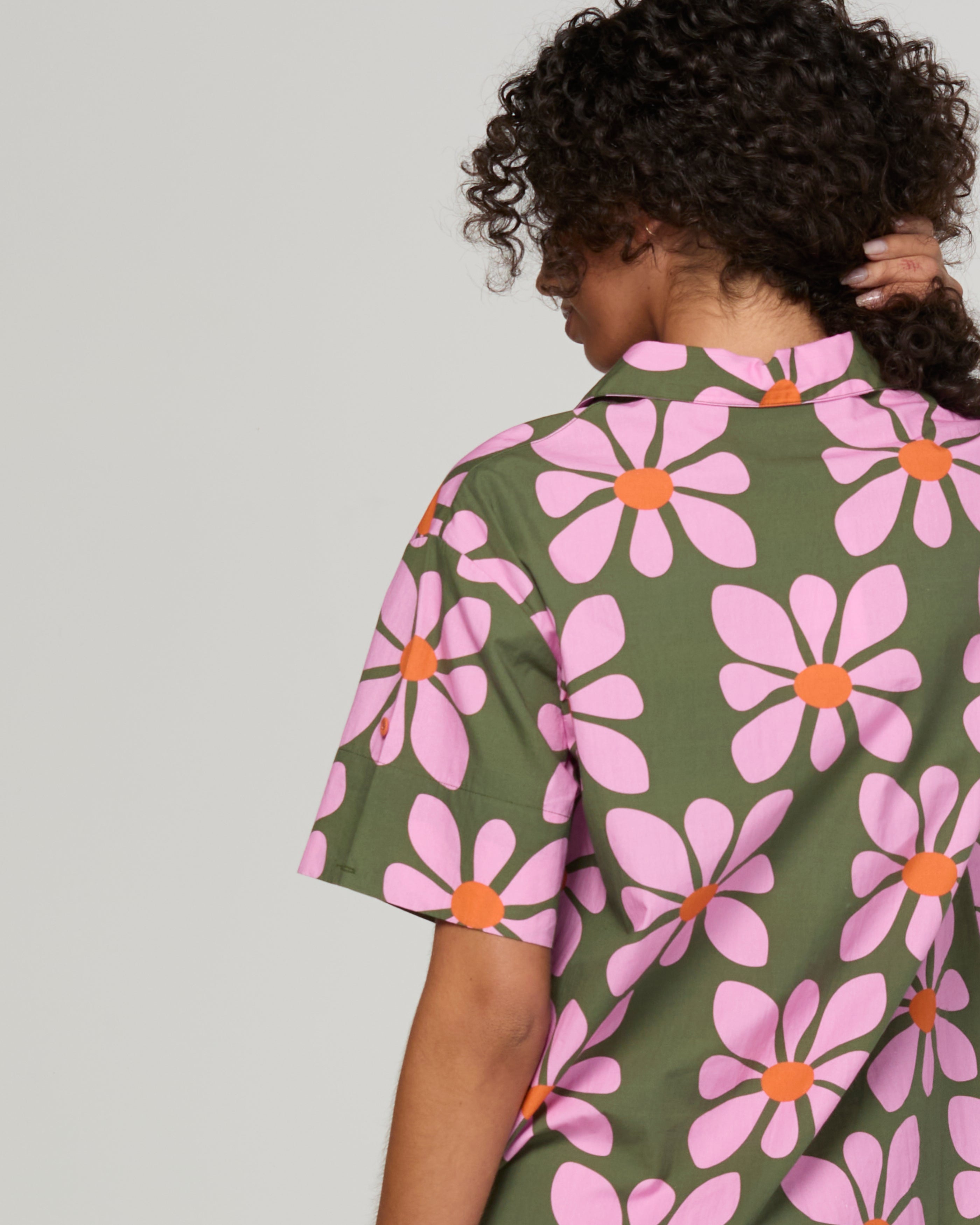 Person wearing a shirt dress with pink floral pattern on a plain background