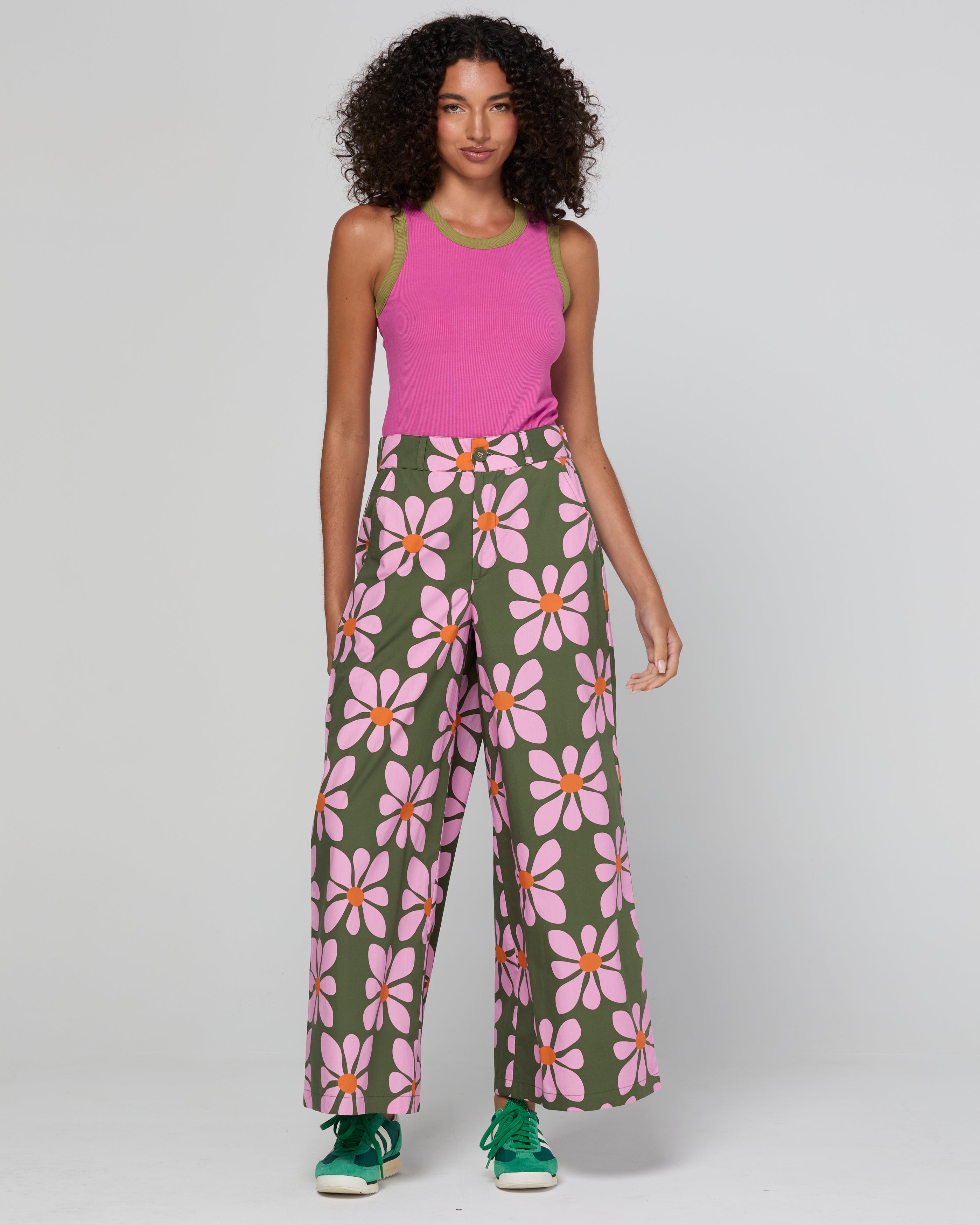Woman wearing a pink sleeveless top and green pants with floral pattern on a white background
