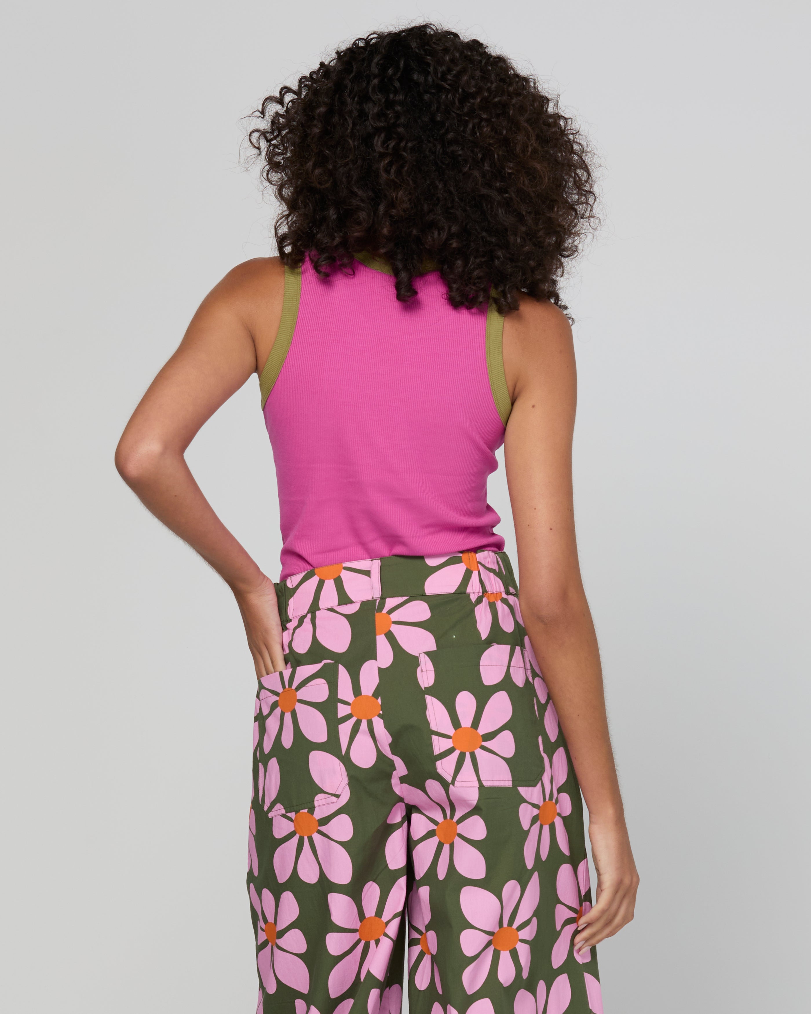 Person wearing a pink sleeveless top and floral pants on a plain background