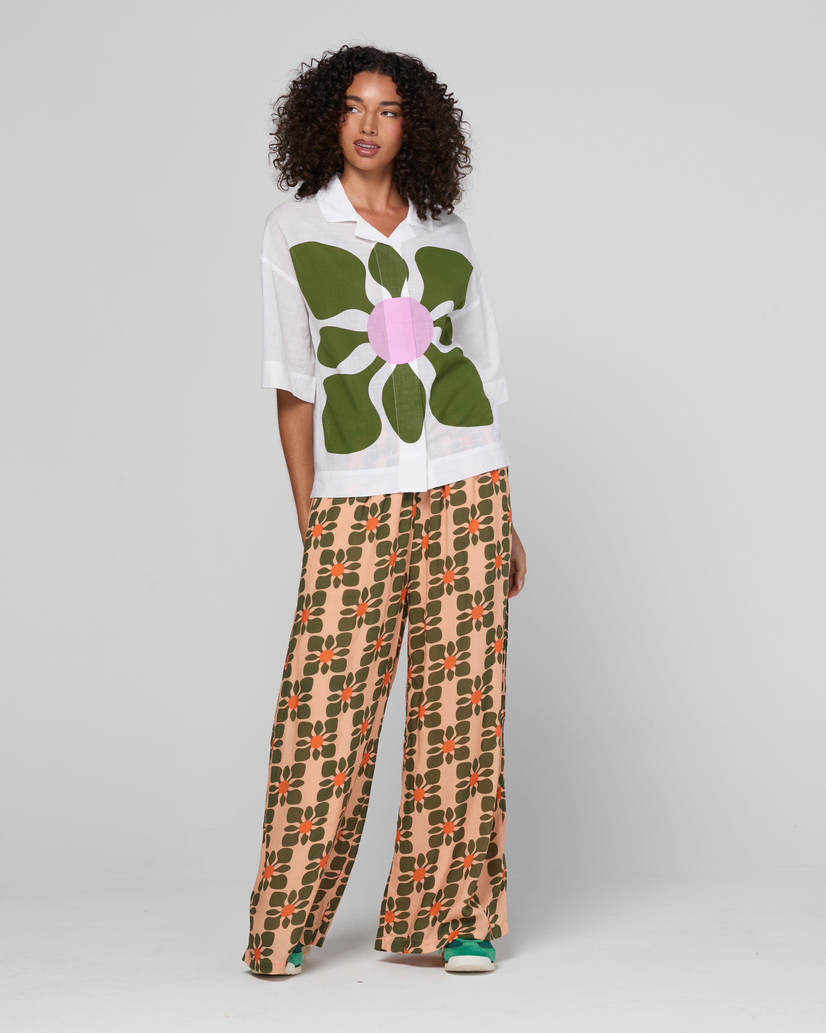 Woman wearing a white shirt with a large green flower design and patterned pants