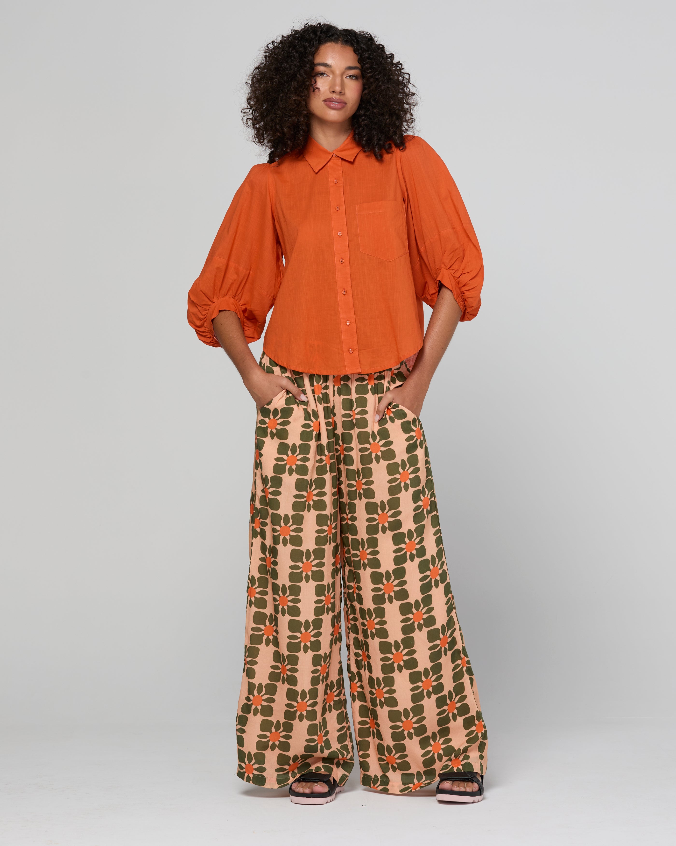 Woman wearing an orange blouse and patterned pants on a white background