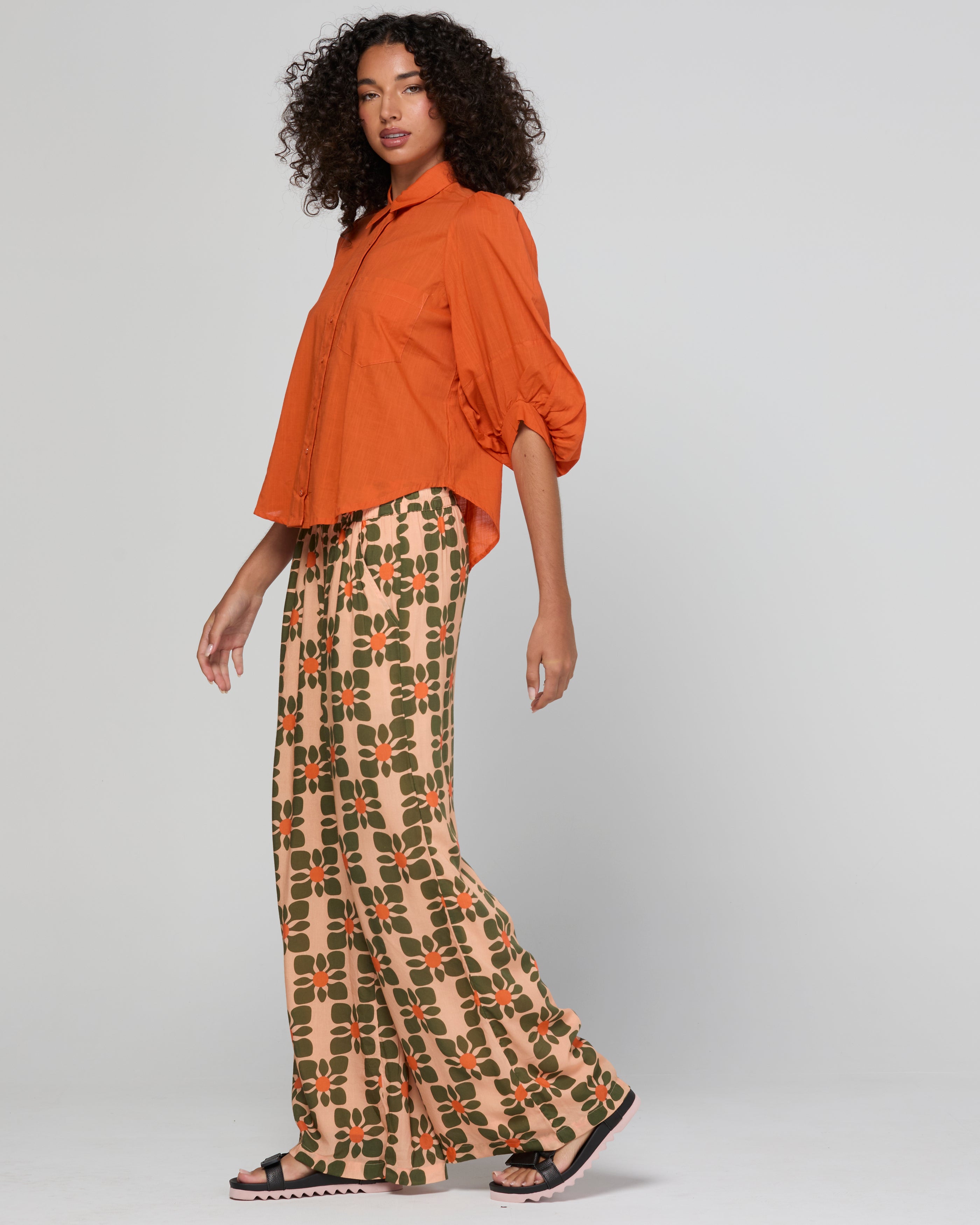 Woman wearing an orange top and patterned pants on a plain background