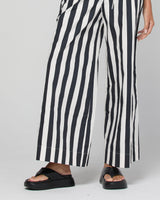 Black and white vertically striped wide-leg pants worn with black platform slide sandals, shown on a model from the waist down against a light gray studio background.