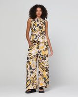 A model wearing a sleeveless top with a wide-leg pant and a peplum waist, featuring a yellow, black, and white paisley floral pattern, photographed against a light gray studio background.