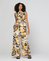A woman modeling a top, wide-leg pant with a bold abstract pattern in black, yellow, and cream, set against a plain light gray studio background.