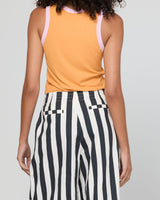 A person shown from the back wearing a sleeveless orange top with light pink shoulder straps and black-and-white vertically striped pants against a light gray studio background.