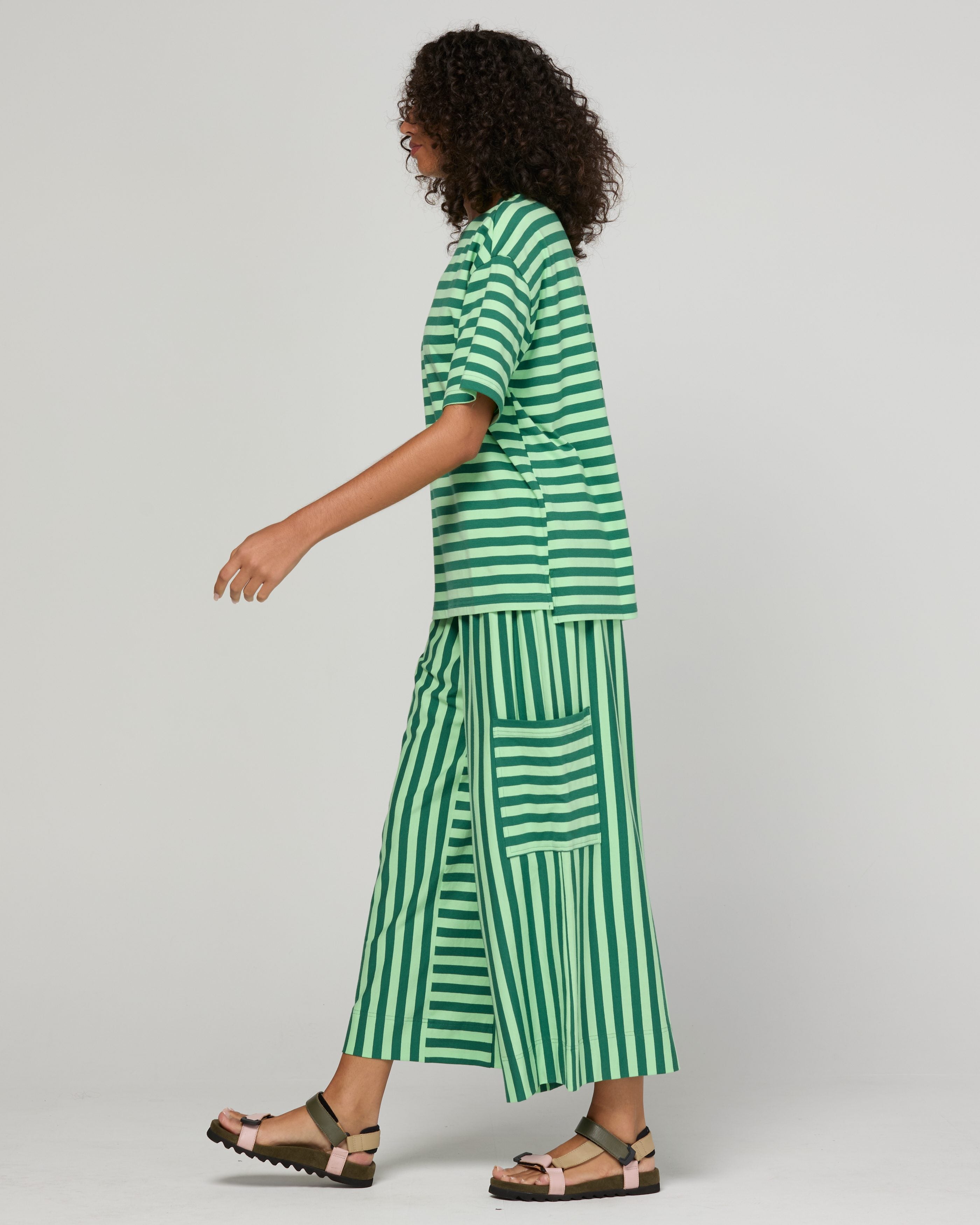 A model wearing a green and white striped matching set consisting of a short-sleeve top and wide-leg pants with vertical stripes, shown from a side profile