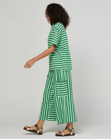 A model wearing a green and white striped matching set consisting of a short-sleeve top and wide-leg pants with vertical stripes, shown from a side profile