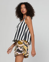 A woman modeling a sleeveless top and shorts set against a plain light gray studio background. The top has vertical black and white stripes, while the shorts feature a multicolor paisley and floral pattern in yellow, brown, black, and white.