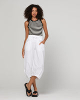 Woman wearing a black and white striped tank top and white pants on a gray background