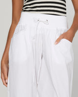 White wide-leg drawstring pants with side pockets, shown on a model wearing a black and white striped top against a light gray background.
