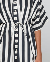 Close-up of a black and white vertically striped short-sleeve shirt dress with a drawstring waist and button front, worn by a model.