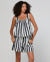 A woman modeling a matching two-piece set consisting of a sleeveless top and shorts, both featuring a bold black and white vertical stripe pattern, set against a plain light gray studio background.