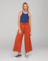 Woman wearing a blue tank top and orange-colored wide-leg pants on a gray background