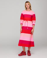Woman wearing a long-sleeved pink and red striped midi dress on a gray background