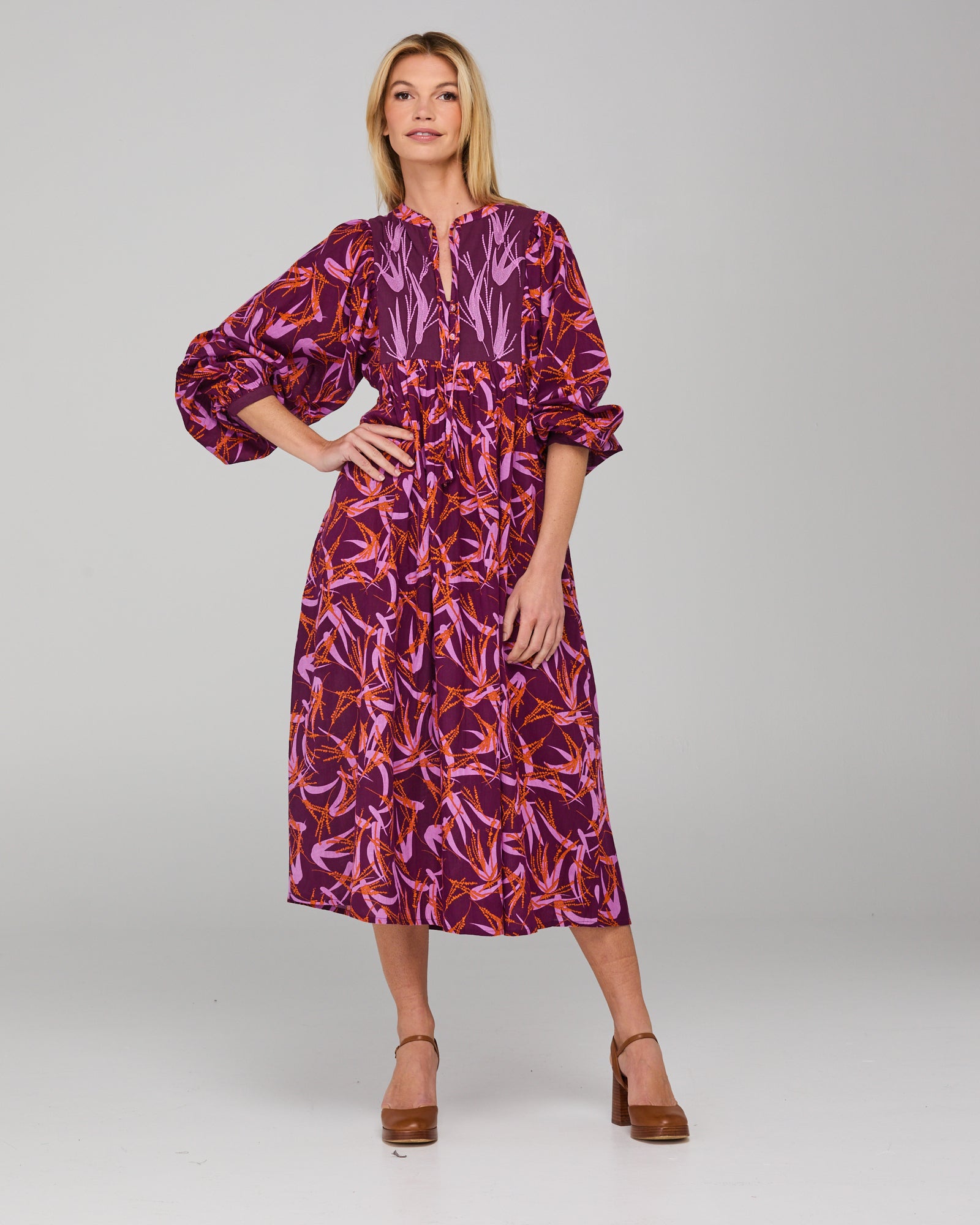 Woman wearing a purple and orange patterned midi dress with long sleeves on a gray background