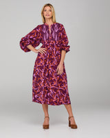 Woman wearing a purple and orange patterned midi dress with long sleeves on a gray background