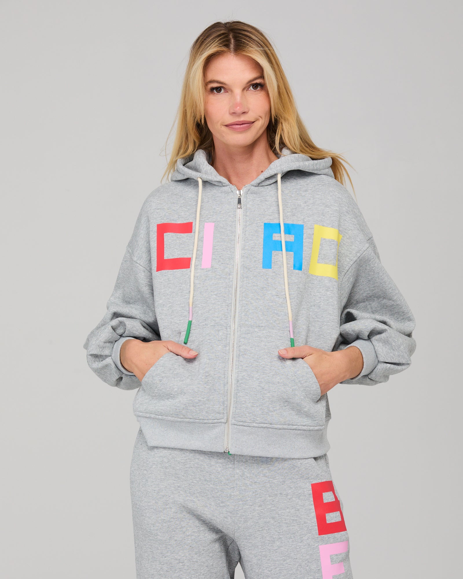 Person wearing a gray hoodie with colorful letters and matching pants on a plain background