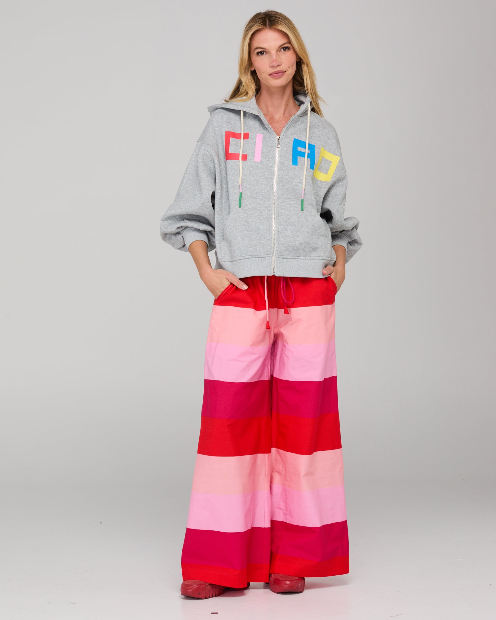 Woman wearing a gray hoodie with colorful letters and pink and red striped pants on a white background