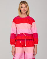 Woman wearing a red and pink striped long sleeved top on a gray background