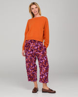 Woman wearing an orange jumper and purple and orange patterned pants on a gray background