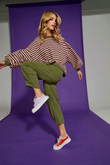 Woman posing in a striped sweater and green pants against a purple backdrop