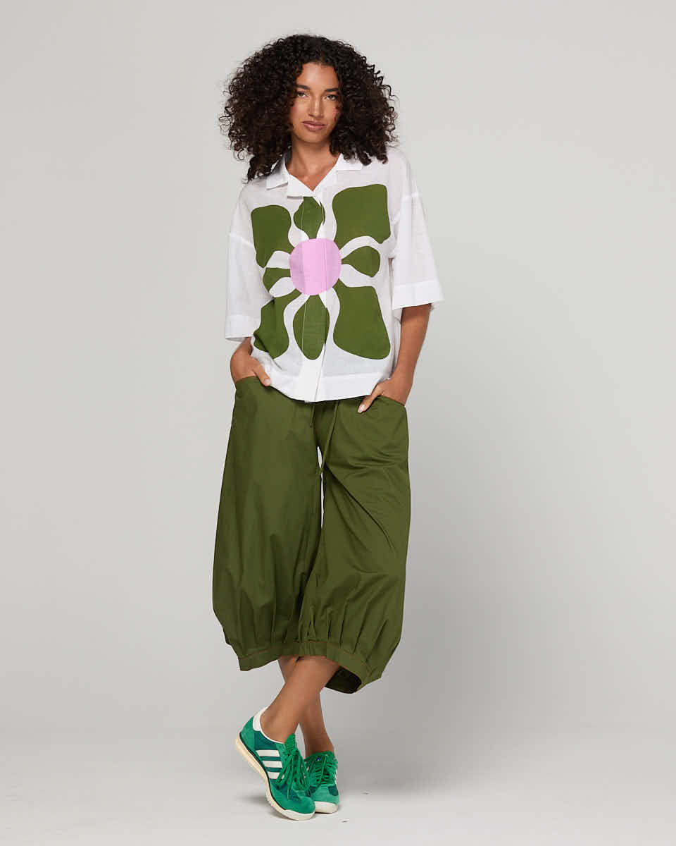 Person wearing a white shirt with a large green flower design and green pants on a plain background