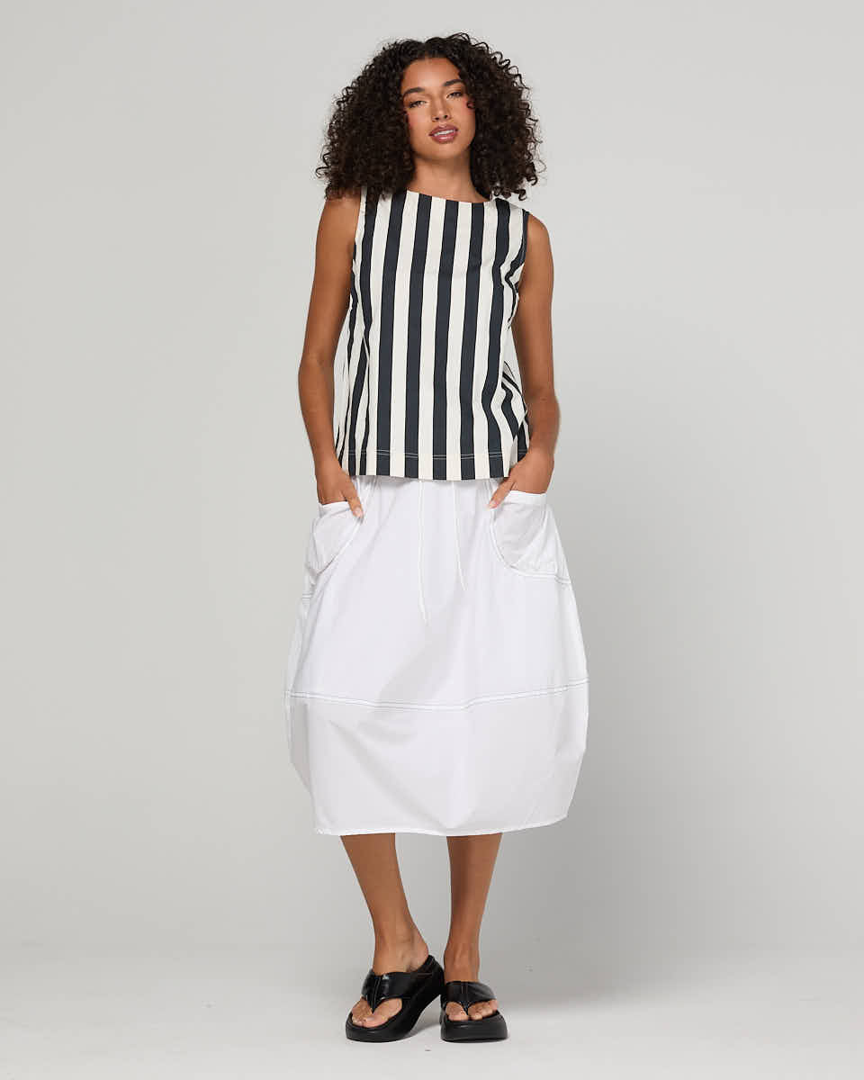 Woman wearing a black and white striped sleeveless top with a white skirt on a plain background
