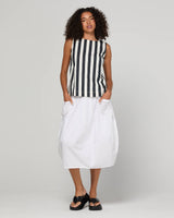 Woman wearing a black and white striped sleeveless top with a white skirt on a plain background