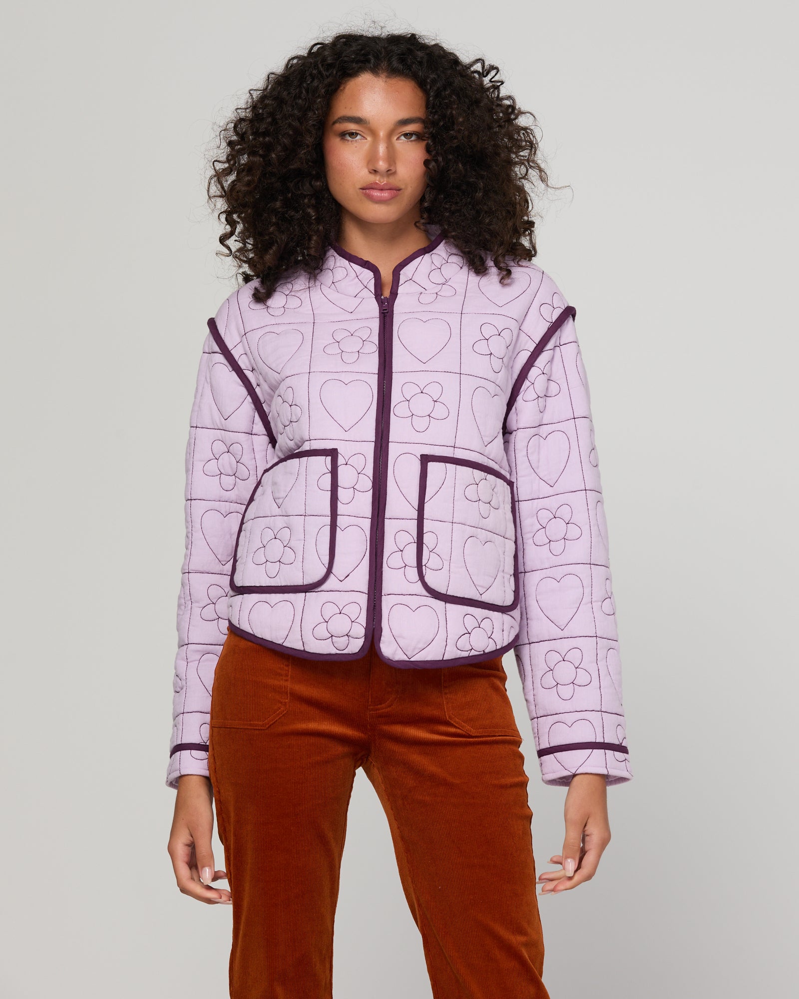 Woman wearing a lilac purple quilted jacket with heart patterns and rust-coloured cord pants