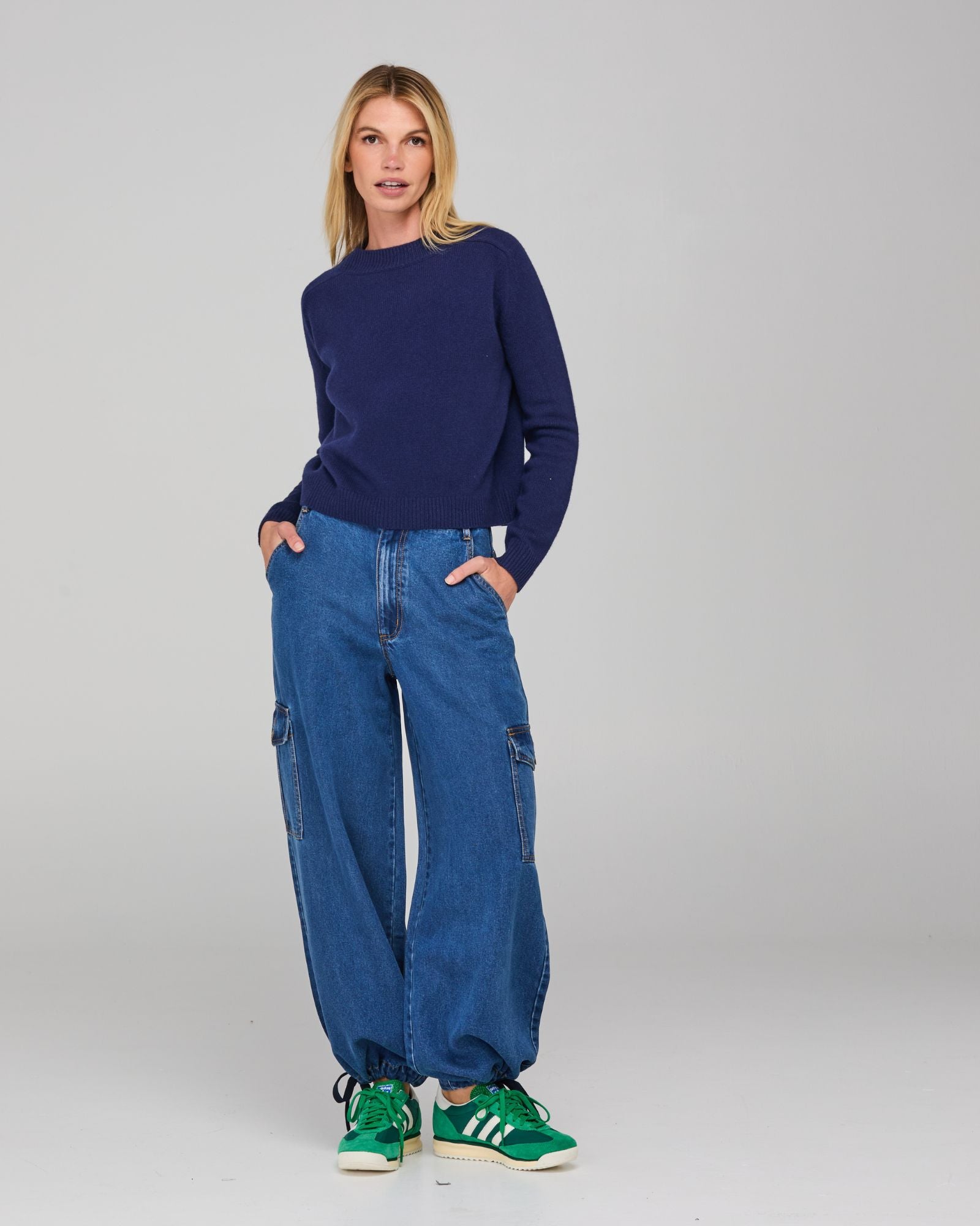 Woman wearing a navy sweater and relaxed denim cargo pants on a gray background